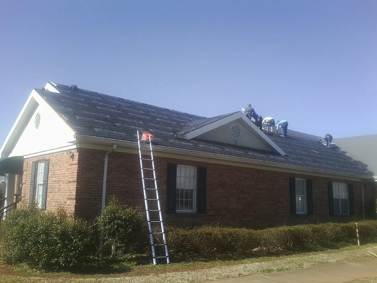 Crew tearing shingles off a brick ranch roof with a ladder set — Metal Roof Repair work by our crew in Azusa