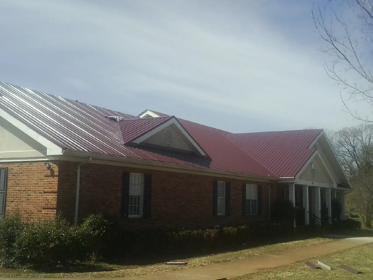 Red metal roof with gabled entries on a long brick building, from a Hail Damage Roof Repair job in Azusa