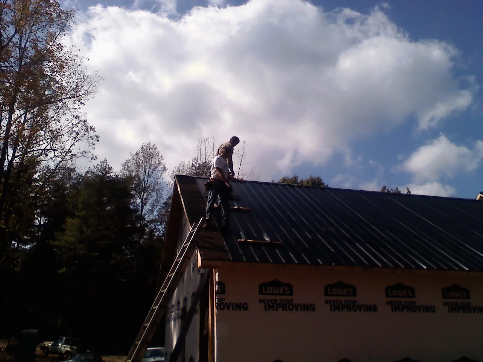 Roofer fastening dark metal panels high against a cloudy sky, from a Roof Inspection job in Azusa