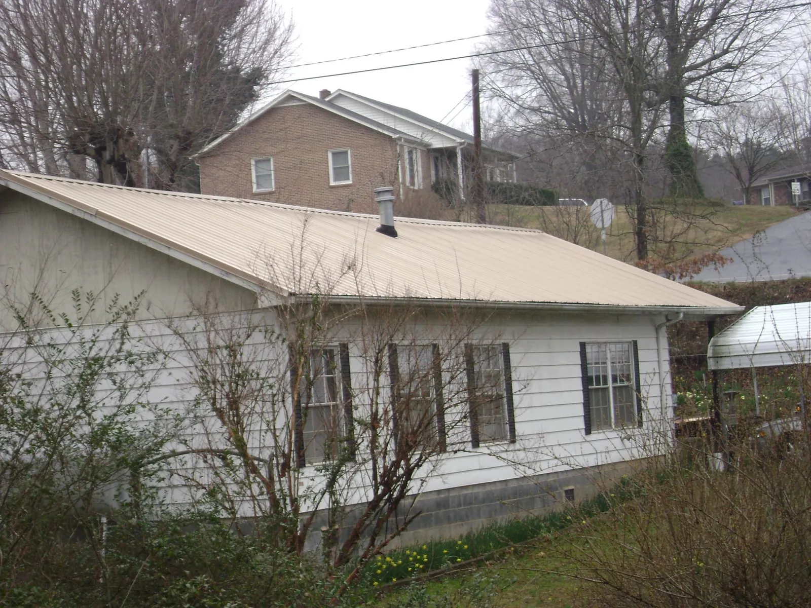 Tan metal roof on a white sided house set into a hillside — Commercial Roofing by Roofing Brothers in Azusa